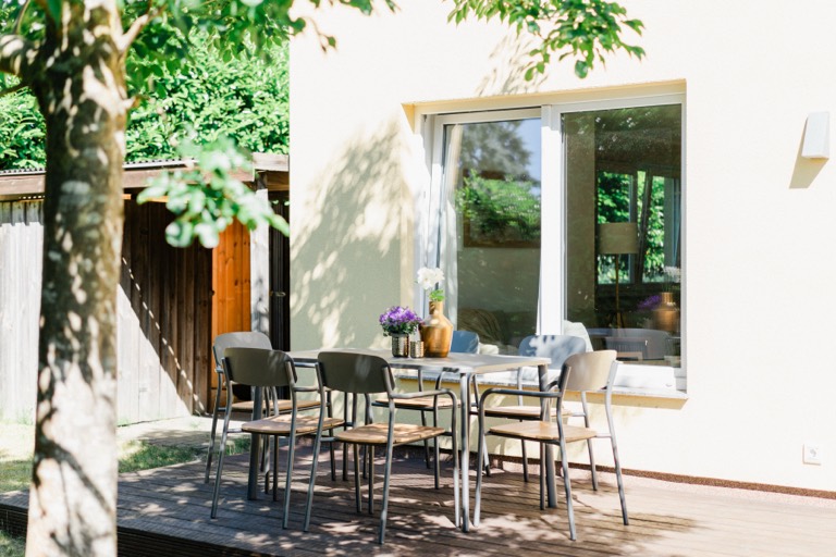 Terrasse mit Esstisch und Stühlen im Schatten eines Baumes